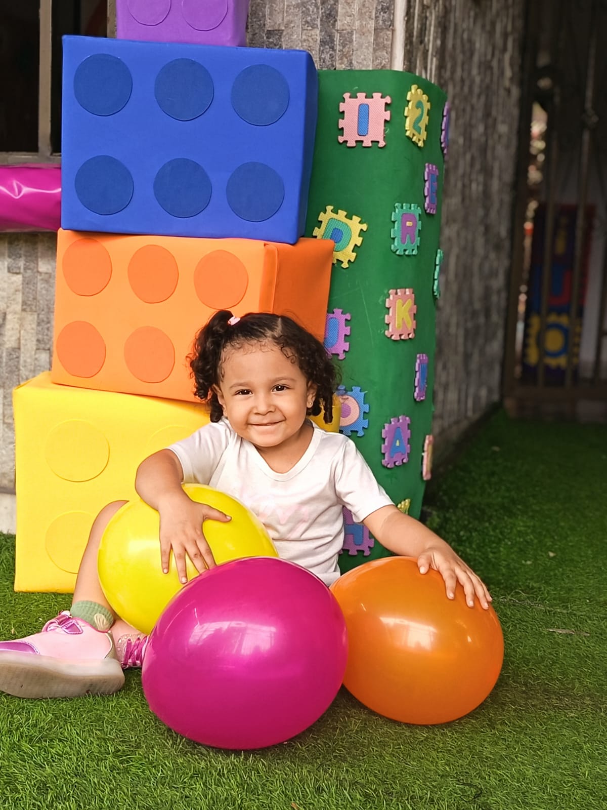 Niña sonriente rodeada de globos de colores y bloques gigantes